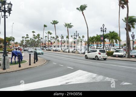 Hauptstraße mit neuen Autos, Palmen und Wanderern in Oranjestad auf Aruba. Stockfoto