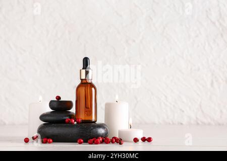 Komposition mit einer Flasche natürlichen ätherischen Öls, Spa-Steinen, brennenden Kerzen und Weißdorn auf hellem Holztisch Stockfoto