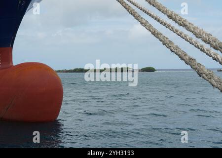 Die Kopflinien kommen vom Bug eines Containerschiffs mit blauem Rumpf und rotem Knollenbogen und durchqueren das panama-Bollwerk. Stockfoto
