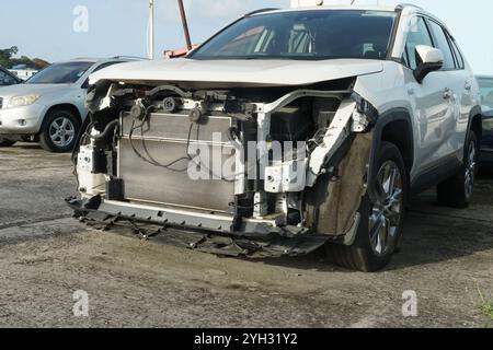 Der Frontgrill und die Motorhaube des weißen Fahrzeugs sind beschädigt, und Kotflügel, Stoßfänger, Halogenleuchte und Motorabdeckung fehlen. Stockfoto