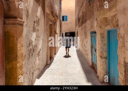 Eine Person, junger Erwachsener männlich, Besichtigungstour durch eine enge Gasse in Medina Essaouira, Marokko, Gebäude mit blau lackierten Türen Stockfoto