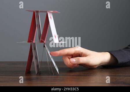 Frau zerstört Haus der Spielkarten am Holztisch vor grauem Hintergrund, Nahaufnahme Stockfoto