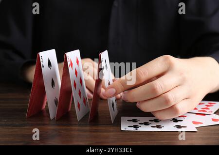 Frau baut Haus mit Spielkarten an Holztisch, Nahaufnahme Stockfoto