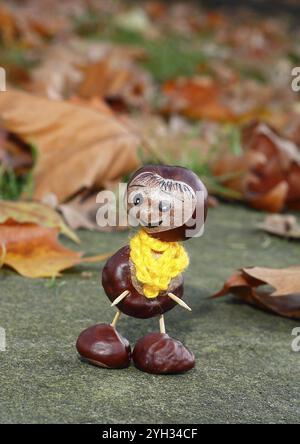 Lustige Kastanienfigur mit gelbem Schal an der Wand in Herbstlaub, Nordrhein-Westfalen, Deutschland, Europa Stockfoto