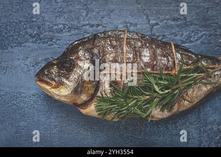 Dorado Fisch, heiß geräuchert, mit einem Zweig Rosmarin, mit einem Seil gebunden, auf blauem Hintergrund, Blick von oben, geräucherter Fisch, Nahaufnahme, keine Leute Stockfoto