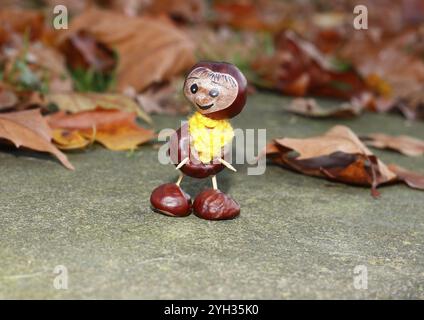 Lustige Kastanienfigur mit gelbem Schal an der Wand in Herbstlaub, Nordrhein-Westfalen, Deutschland, Europa Stockfoto