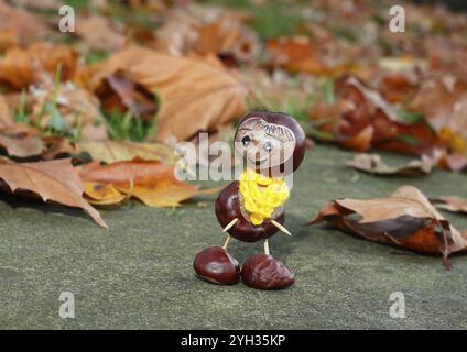 Lustige Kastanienfigur mit gelbem Schal an der Wand in Herbstlaub, Nordrhein-Westfalen, Deutschland, Europa Stockfoto