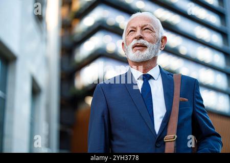 Porträt eines bärtigen Geschäftsmannes mit Laptoptasche, der wegblickt, während er außerhalb des Büros steht Stockfoto