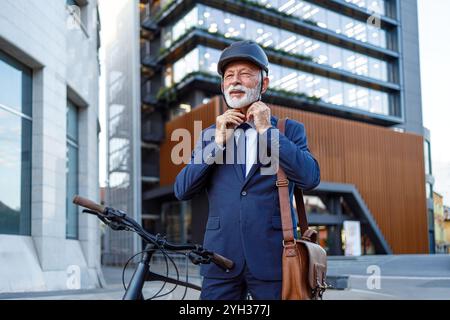 Porträt eines bärtigen Geschäftsmannes, der seinen Fahrradhelm anzieht, während er in der Stadt am Fahrrad steht Stockfoto