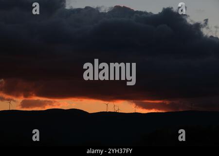 Windturbinen oben auf dem Hügel unter den riesigen Wolken während Sonnenuntergang. Foto des Umweltschutzkonzepts. Stockfoto