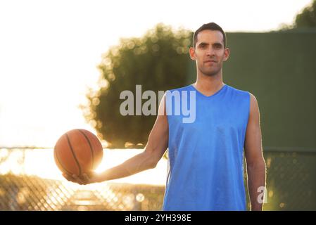 Athlet Mann mit Basketball Ball stehend auf Spielplatz bei Sonnenuntergang Stockfoto