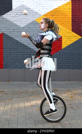 Mädchen Clown fährt auf einem Einrad und jongliert mit Bällen vor der farbenfrohen Wand draußen Stockfoto