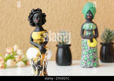 Zwei Statuetten schwarzer Frauen in traditionellen gelben und grünen brasilianischen Kostümen. Orangefarbener Wandhintergrund und Vasen von Sukkulenten. Stockfoto