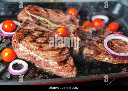 Steaks werden mit Tomaten, Zwiebeln und Rosmarin gegrillt. Hochwertige Fotos Stockfoto