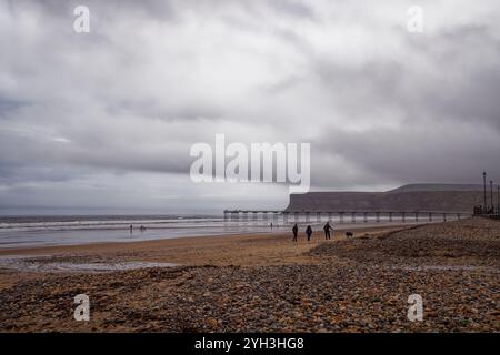 Leute laufen an einem regnerischen Strand am Saltburn Pier, England. Stockfoto