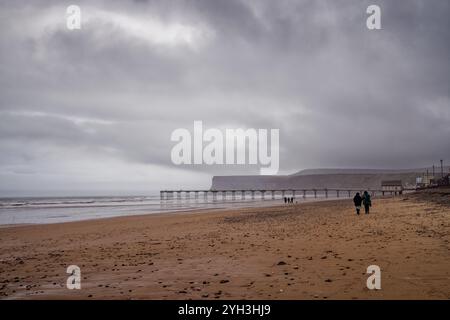 Leute laufen an einem regnerischen Strand am Saltburn Pier, England. Stockfoto