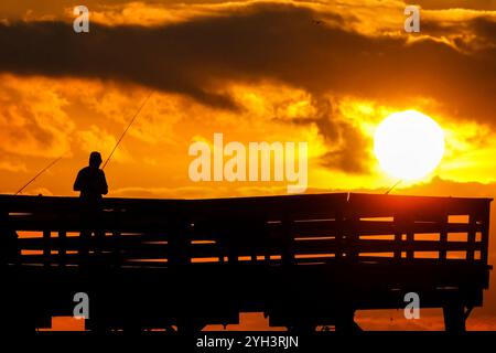 Isle Of Palms, Usa. November 2024. Ein einsamer Fischer, der vom Sonnenaufgang umrahmt wird, steht am Angelpier der Isle of Palms, während die Sonne am 9. November 2024 in Isle of Palms, South Carolina, durch die Morgenwolken über dem Atlantik bricht. Sonniges Wetter in den 70er Jahren wird für das niedere Land für die nächsten zehn Tage prognostiziert. Quelle: Richard Ellis/Richard Ellis/Alamy Live News Stockfoto