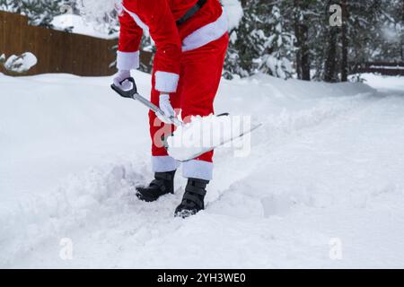 Der Weihnachtsmann reinigt im Winter draußen nach einem Schneefall Schnee mit Schaufel. Die Straßen im Dorf zu reinigen, die Passage für Autos freizumachen, schwierig Stockfoto