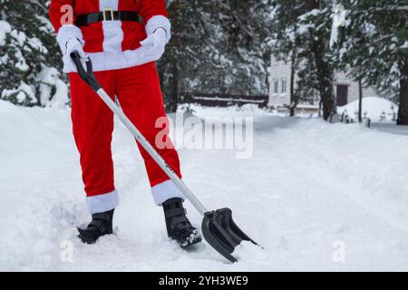 Der Weihnachtsmann reinigt im Winter draußen nach einem Schneefall Schnee mit Schaufel. Die Straßen im Dorf zu reinigen, die Passage für Autos freizumachen, schwierig Stockfoto