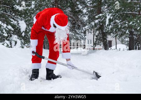 Der Weihnachtsmann reinigt im Winter draußen nach einem Schneefall Schnee mit Schaufel. Die Straßen im Dorf zu reinigen, die Passage für Autos freizumachen, schwierig Stockfoto