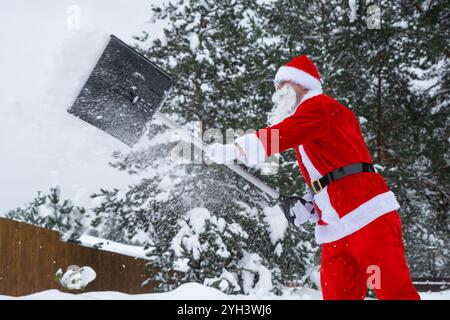 Der Weihnachtsmann reinigt im Winter draußen nach einem Schneefall Schnee mit Schaufel. Die Straßen im Dorf zu reinigen, die Passage für Autos freizumachen, schwierig Stockfoto