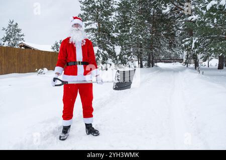 Der Weihnachtsmann reinigt im Winter draußen nach einem Schneefall Schnee mit Schaufel. Die Straßen im Dorf zu reinigen, die Passage für Autos freizumachen, schwierig Stockfoto