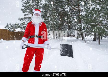 Der Weihnachtsmann reinigt im Winter draußen nach einem Schneefall Schnee mit Schaufel. Die Straßen im Dorf zu reinigen, die Passage für Autos freizumachen, schwierig Stockfoto