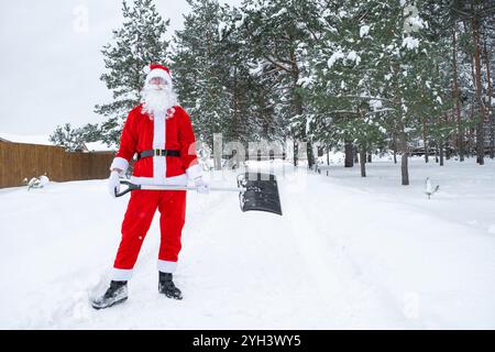 Der Weihnachtsmann reinigt im Winter draußen nach einem Schneefall Schnee mit Schaufel. Die Straßen im Dorf zu reinigen, die Passage für Autos freizumachen, schwierig Stockfoto