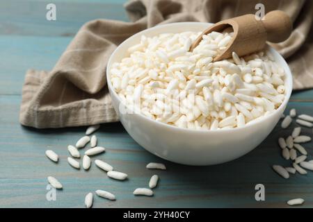 Puffreis in Schüssel und Löffel auf hellblauem Holztisch, Nahaufnahme Stockfoto