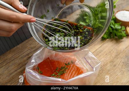 Frau mit Sojamarinade und Lachsfilet in Plastiktüte am Holztisch, Nahaufnahme Stockfoto