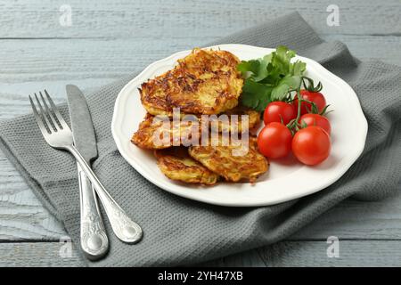 Köstliche Kartoffelpfannkuchen mit Tomaten und Petersilie auf grauem Holztisch, Nahaufnahme Stockfoto