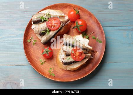 Köstliche Sandwiches mit Sprotten, Mikrogrün und Tomaten auf hellblauem Holztisch, Blick von oben Stockfoto