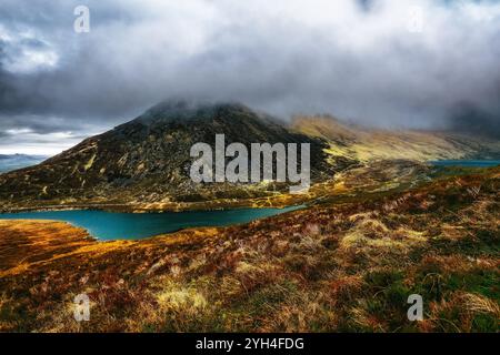 Eine malerische Aussicht auf eine Bergkette mit einem Vorboden aus trockenem Gras, einem gekrümmten See im Tal und einem Hügel, der in Nebel gehüllt ist. Stockfoto