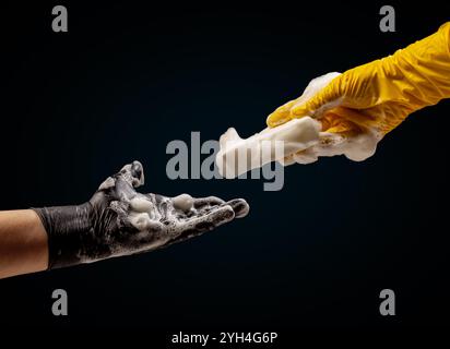 Ein Paar Hände, eine trägt einen schwarzen Schutzhandschuh und die andere einen gelben, tauscht einen Schwamm aus. Der Prozess des Geschirrspülens oder der Reinigung. Stockfoto