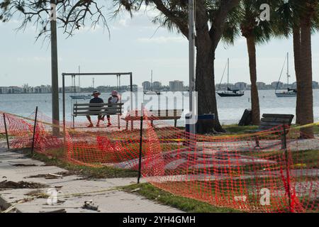 Blick von hinten älteres Paar mit Hüten auf einer Metallschaukel über den Sandstrand hinaus zu Segelbooten am Gulfport Florida Beach. Gebäude und ja Stockfoto