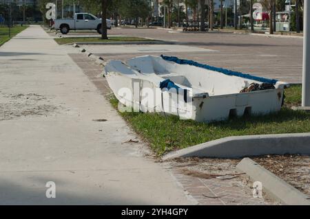 Führende Linien mit Blick auf den Bürgersteig mit einem kleinen weißen Ruderboot. Grünes Gras und Bäume an der Seite. Gulfport Florida Beach. Auf der Boca Ciega Bay nach St. Stockfoto