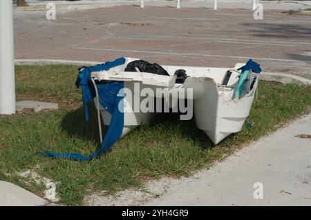 Isolierter Blick auf den Bürgersteig mit einem kleinen weißen Ruderboot. Grünes Gras und Parkplatz hinten. Gulfport Florida Beach. Auf der Boca Ciega Bay nach Stron Stockfoto