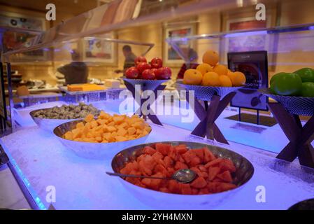 Das Buffet bietet frisches Obst wie Wassermelone und Drachenfrüchte in Eisschalen mit Äpfeln und Orangen in Körben unter kühlem blauem Licht Stockfoto