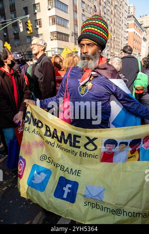 New York, NY, USA. November 2024. Demonstranten aus verschiedenen Gruppen und Einzelpersonen beteiligen sich an der protestmarsch „unsere Zukunft schützen“ in der Nähe des Kolumbus Circle, um gegen die von der neuen Trump-Regierung vorgeschlagene Politik zu protestieren. Ein Mann mit einer bunten Dreadlock-Kappe trägt ein Banner für die SNP BAME, die Schwarze, Asiatische und Minderheitengruppe der SNP, der Scottish National Party. Quelle: Ed Lefkowicz/Alamy Live News Stockfoto