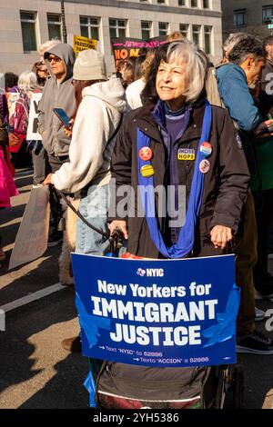 New York, NY, USA. November 2024. Demonstranten aus verschiedenen Gruppen und Einzelpersonen beteiligen sich an der protestmarsch „unsere Zukunft schützen“ in der Nähe des Kolumbus Circle, um gegen die von der neuen Trump-Regierung vorgeschlagene Politik zu protestieren. Eine Frau schiebt einen Walker mit einem Plakat, das die New Yorker für die Gerechtigkeit der Immigranten unterstützt. Quelle: Ed Lefkowicz/Alamy Live News Stockfoto