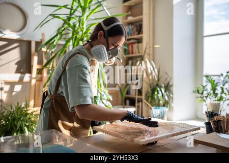 Nahaufnahme einer Künstlerin, die Epoxidharz mit Handschuhen aufträgt, in der Nahaufnahme des Kunststudios. Flüssige Kunst. Stockfoto