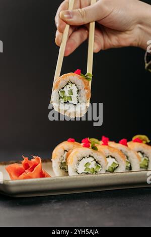 Halten Sie Sushi-Brötchen mit Lachs, Gurke und Frischkäse mit Essstäbchen von Hand Stockfoto