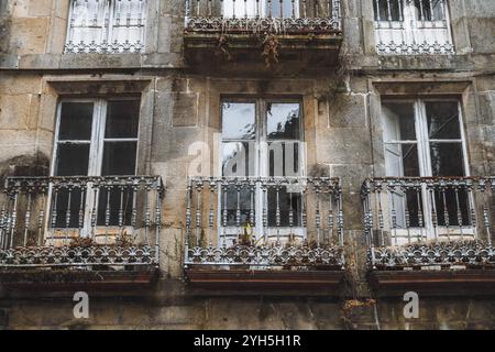 Nahaufnahme einer alten europäischen Gebäudefassade mit verwitterten Steinwänden, rissigen Glasscheiben und kunstvollen schmiedeeisernen Geländern auf einem kleinen Balkon Stockfoto