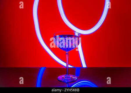 Nahansicht des Cocktailglases mit Eis vor leuchtendem rotem und blauem Neonhintergrund. Stockfoto