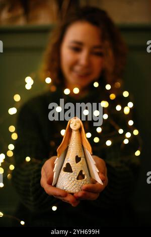 Festliches Weihnachtsbild von Frauenhänden, die Engelsfigur halten. Engel Figur in warmen Weihnachtslichtern, gehalten von einer Frauenhände, die heiter und fest wirkt Stockfoto