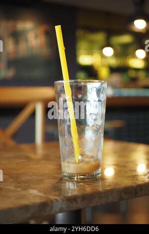 Ein leeres Glas mit gelbem Strohhalm steht auf einem rustikalen Tisch im Café Stockfoto