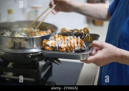 Hände einer Frau, die Essstäbchen benutzt, um gekochte haarige Krabben in einem Dampfgarer aufzuheben. Köstliche Yangcheng-Seekrebse für ein Familienessen. Stockfoto