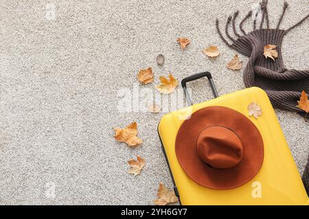 Gelber Koffer mit stilvollem Hut, Strickschal und Herbstlaub auf grauem Teppich. Reisekonzept Stockfoto