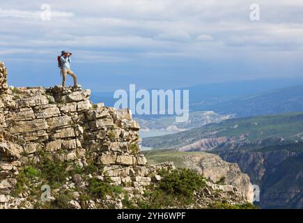 Die junge Fotografin, die am Rande einer Klippe steht, macht Fotos von einer atemberaubenden Berglandschaft Stockfoto