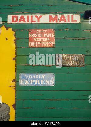 Vintage-Emaille-Schilder, die Daily Express, Daily Mail, Sunday Telegraph und Western Daily Press (Bristol) auf grünem Wetterschild an der Bitton Station anzeigen Stockfoto